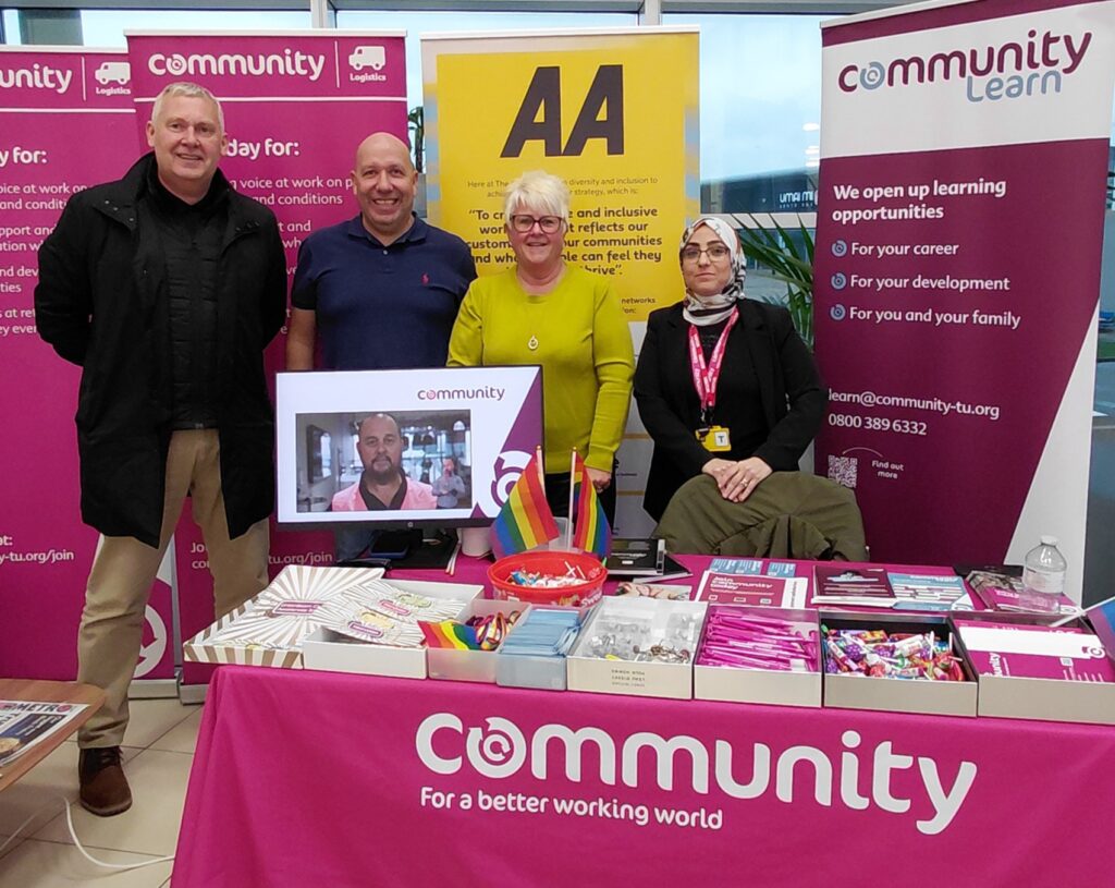 A photograph of Paul Warren, Sean Mallenby, Bev Stafford and Hiba Bayoumi, stood at a Community stand at AA Newcastle.